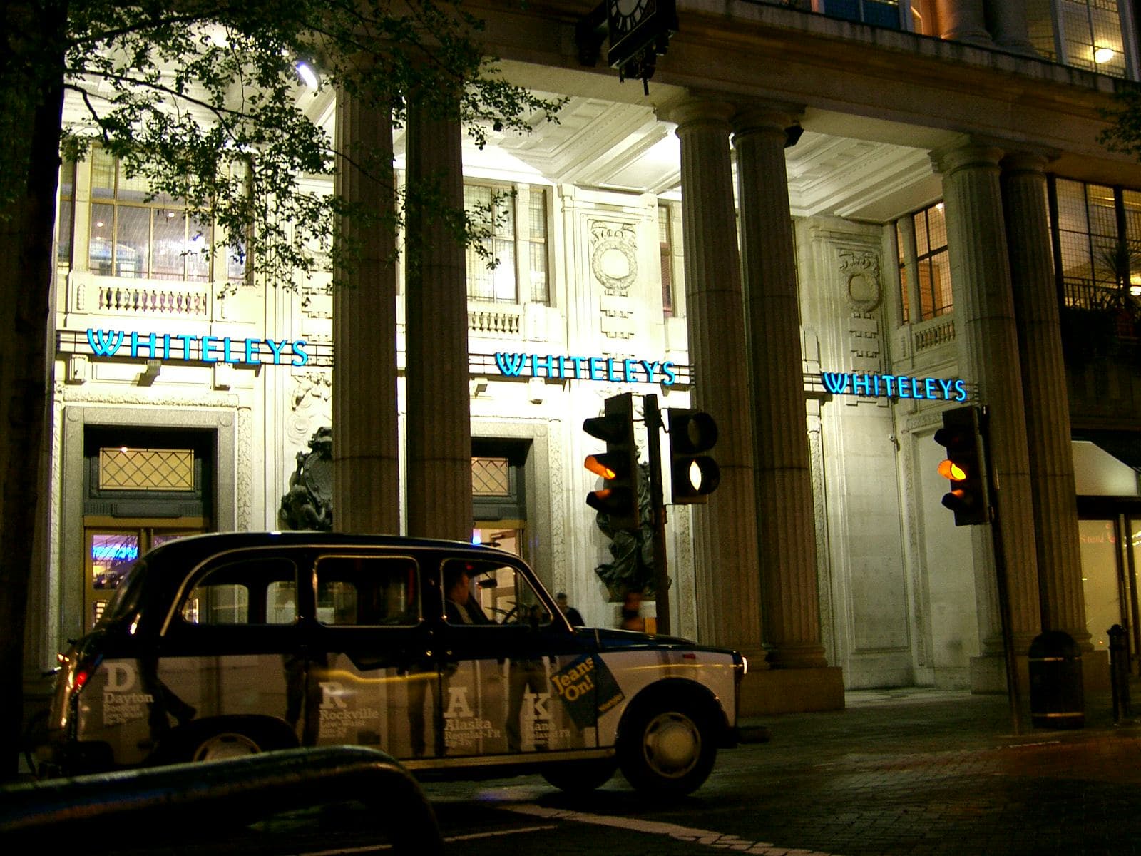 A London black cab passing Whiteleys in Bayswater at 4:04 a.m. under illuminated street lights